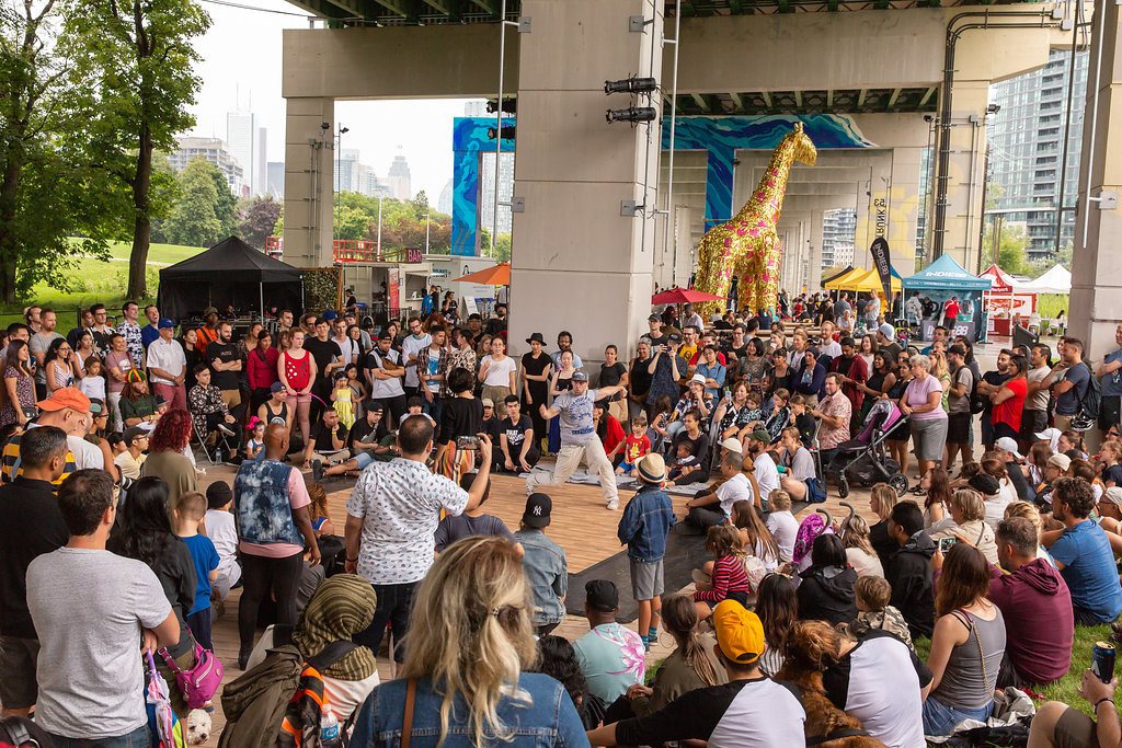 A crowd of people watch a dancer perform outdoors at The Bentway.