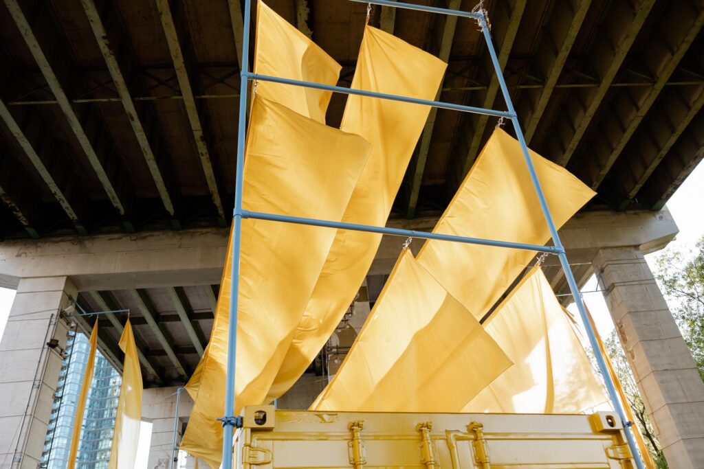 Large sheets of yellow fabric attached to a tall metal frame blowing in the wind.