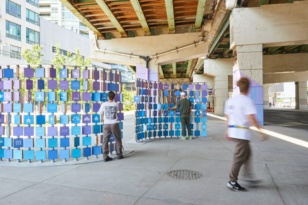 Pedestrians explore a colourful wall under an expressway.