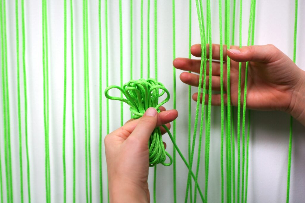 Two hands weaving neon green thread against a white background.