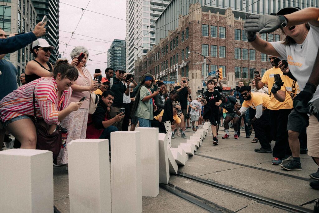 People watching and taking pictures of a line of giant dominoes falling through an intersection in Toronto.