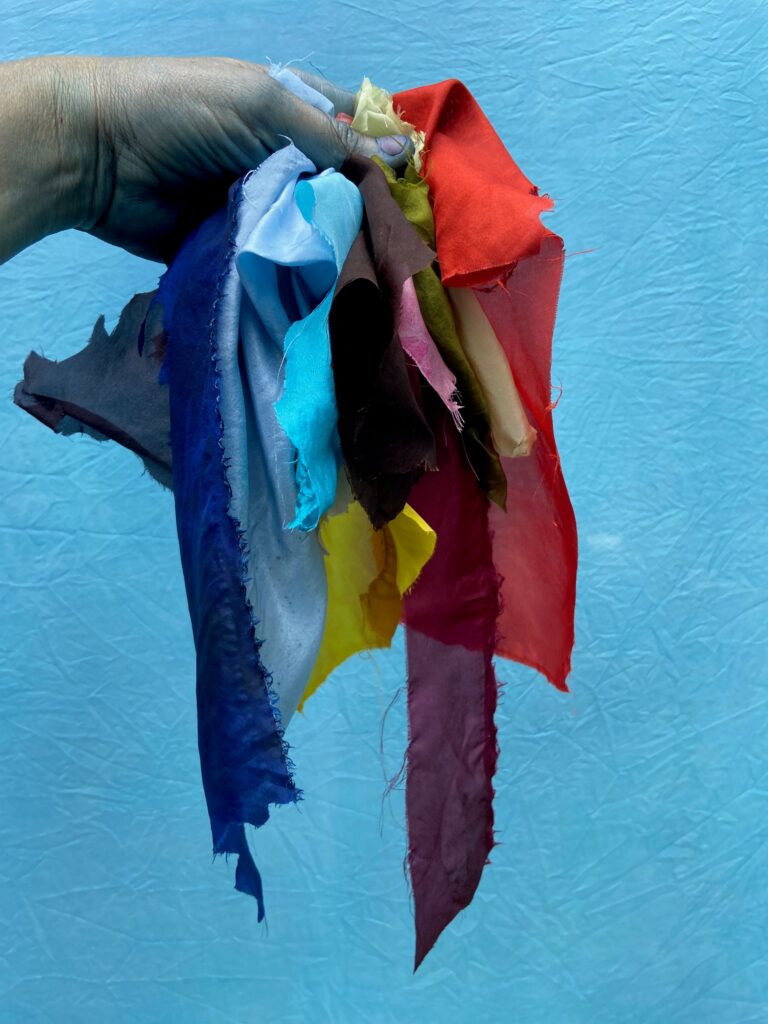 Hand holding a bunch of colourful blue scraps of silk against a bright blue wall.