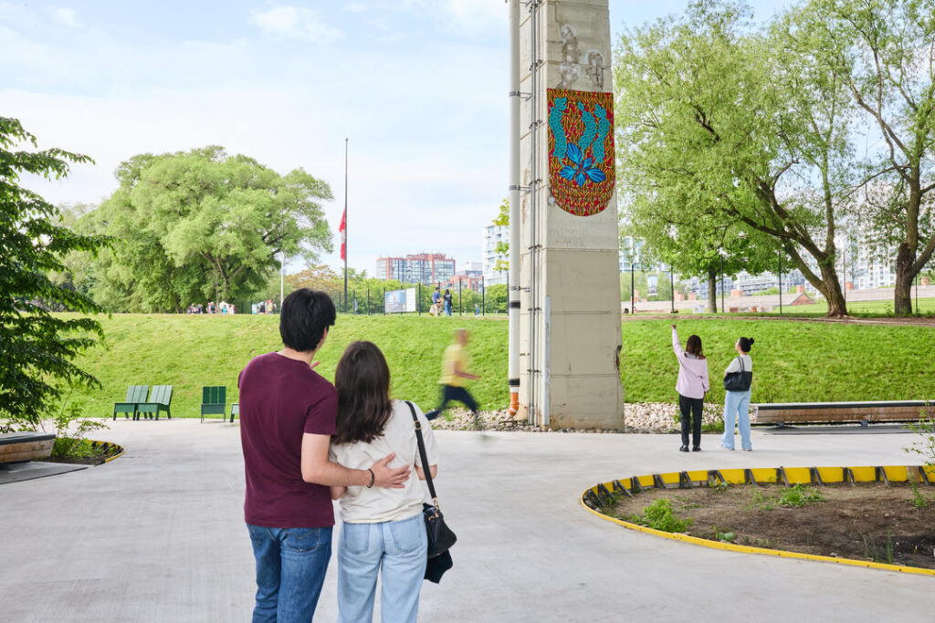 Two pairs of people standing and looking at one of The Bentway's art installations on a concrete pillar, one from close up and one from a distance.