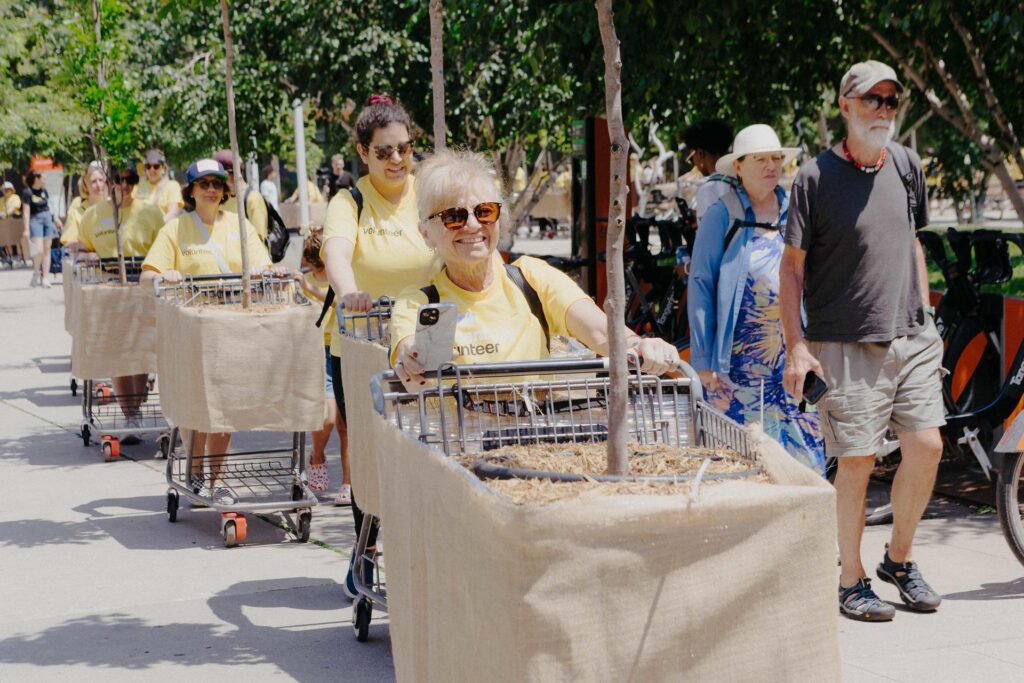 Line of people pushing shopping carts carrying small trees as part of The Bentway's Moving Forest exhibition. 